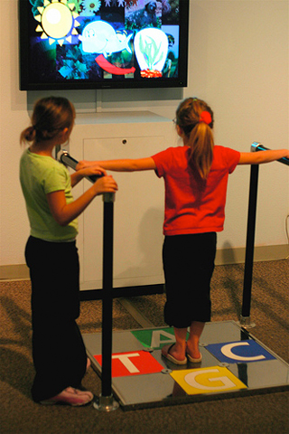 A child stands on a pad labeled A, T, C, G in front of a TV screen.