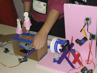 A photo of a contraption made of plastic parts, wires, motors, Popsicle sticks and springs.