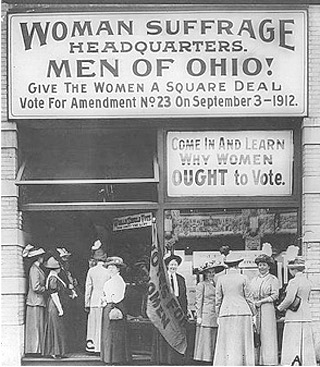 A black and white photo from 1912 shows the outside of the woman suffrage headquarters. Signs urge the men of Ohio to back Amendment 23.