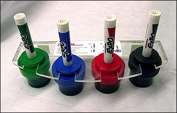 Four white board markers in a refill station.