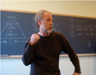 A bearded man moves his fist in front of a chalkboard discussing key story elements and their sequence.