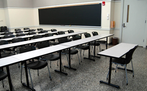 Medium-sized classroom with rows of tables and a blackboard on the side.